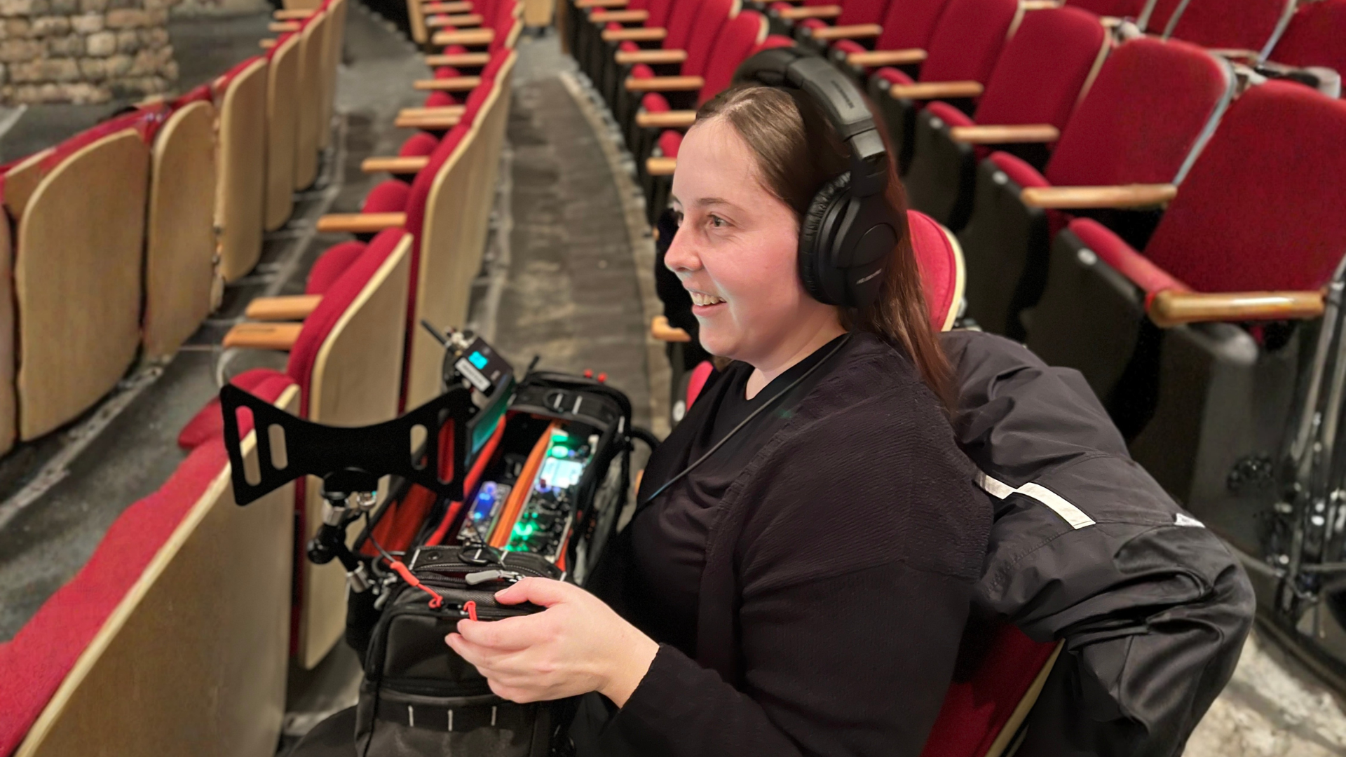 Woman wearing headphones operating a camera rig in a theater with red seats