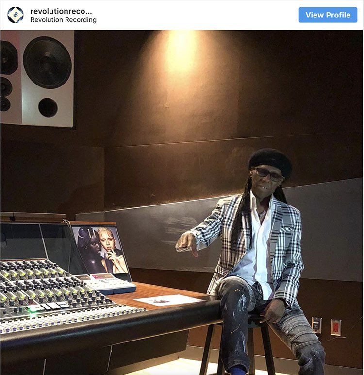 A man is sitting on a stool in front of a keyboard in a recording studio.