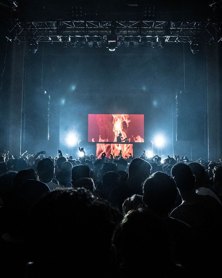 A crowd of people watching a concert with a large screen on the stage