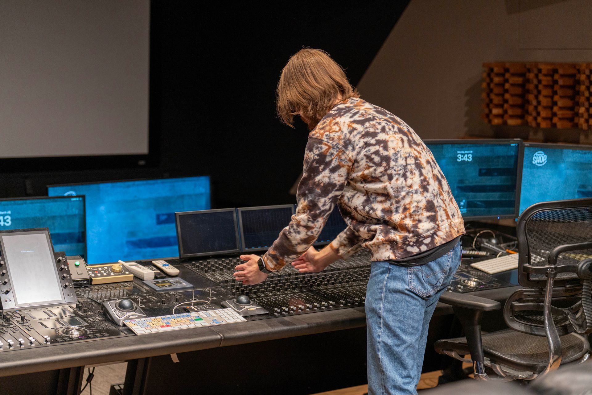 Gabriel Packer adjusting audio mixing console in a recording studio with multiple monitors and equipment.