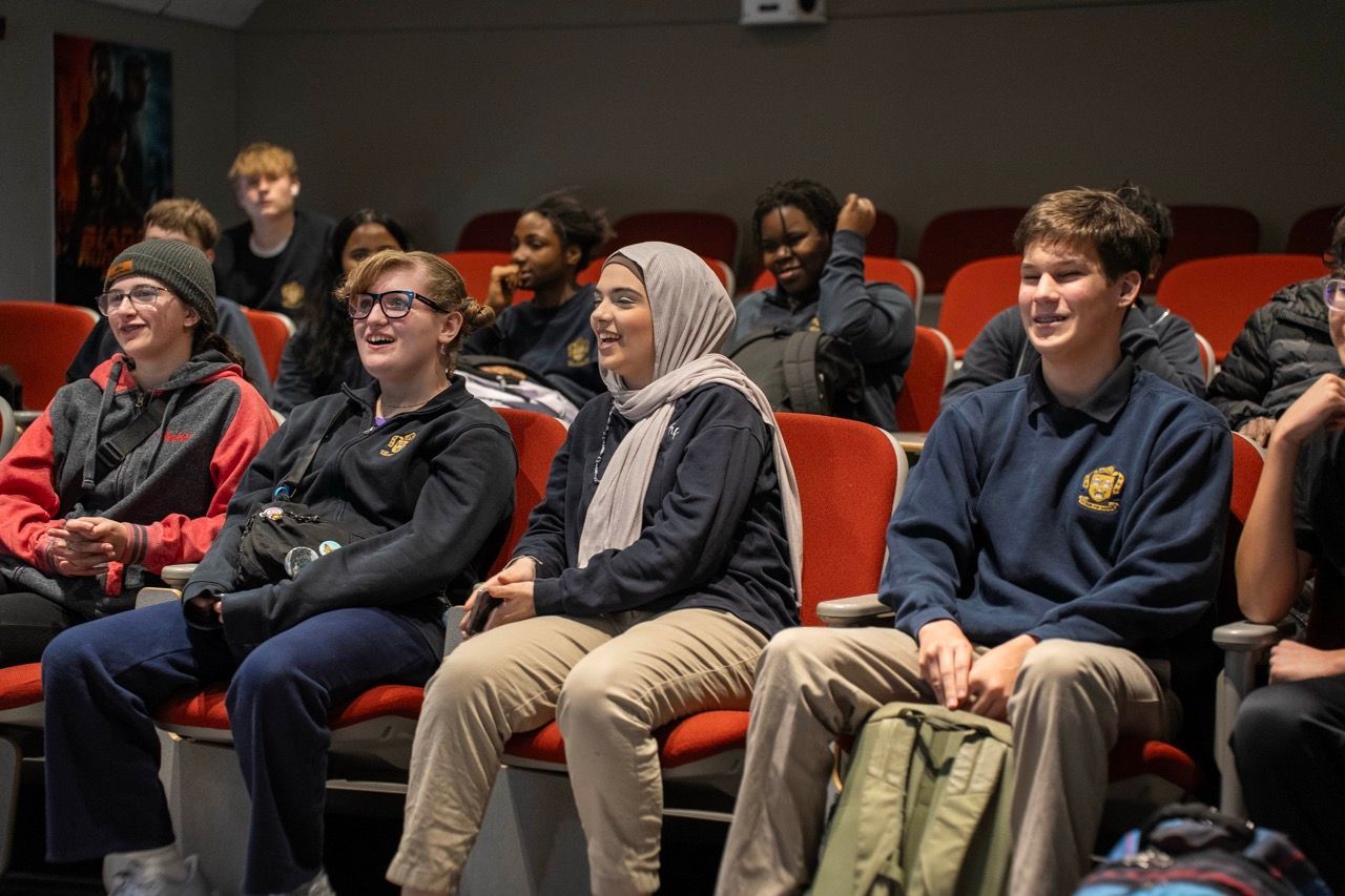 A group of students sitting in rows in a theater, listening attentively.