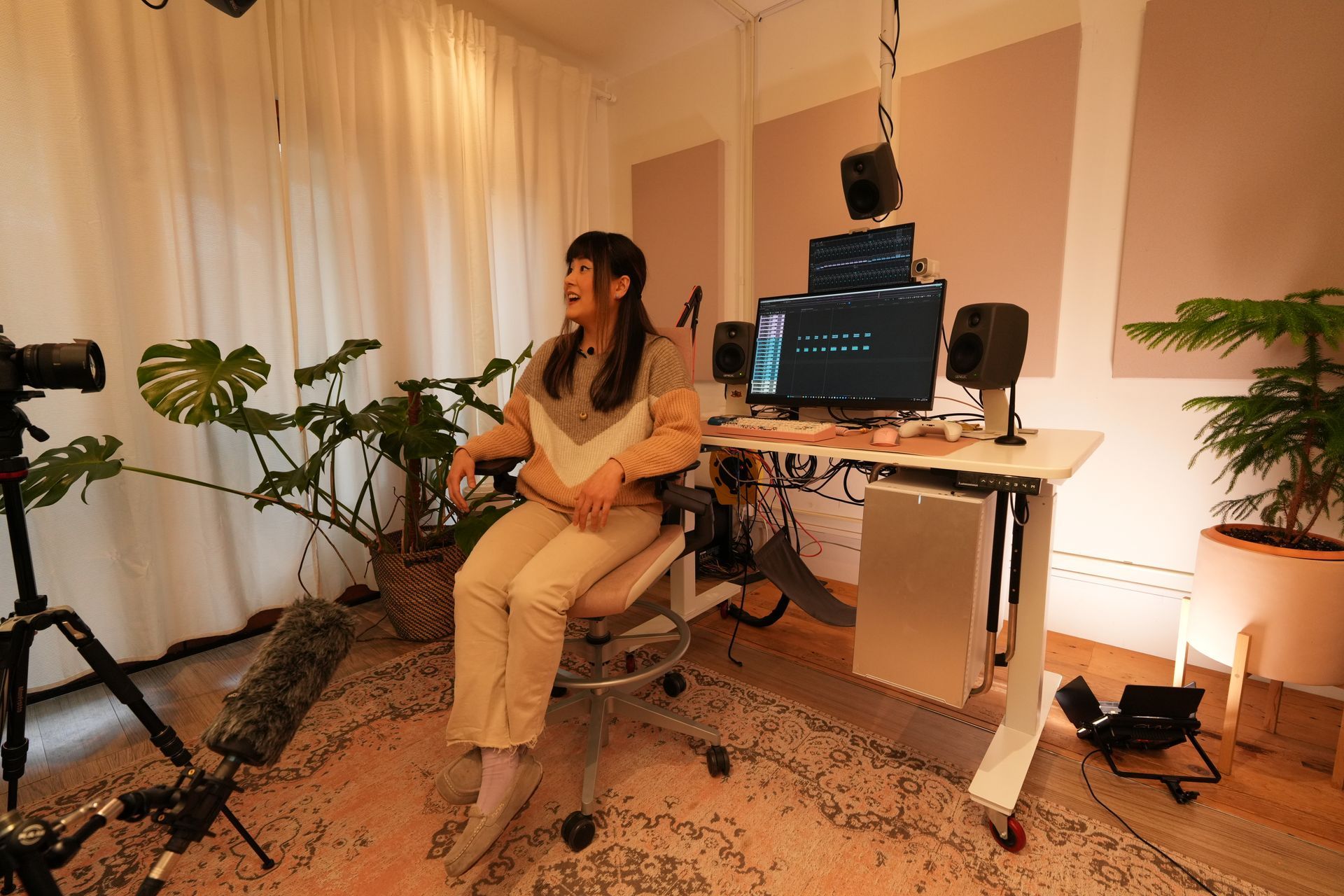 Michelle seated in a cozy home studio, singing into a microphone beside a computer and plants.