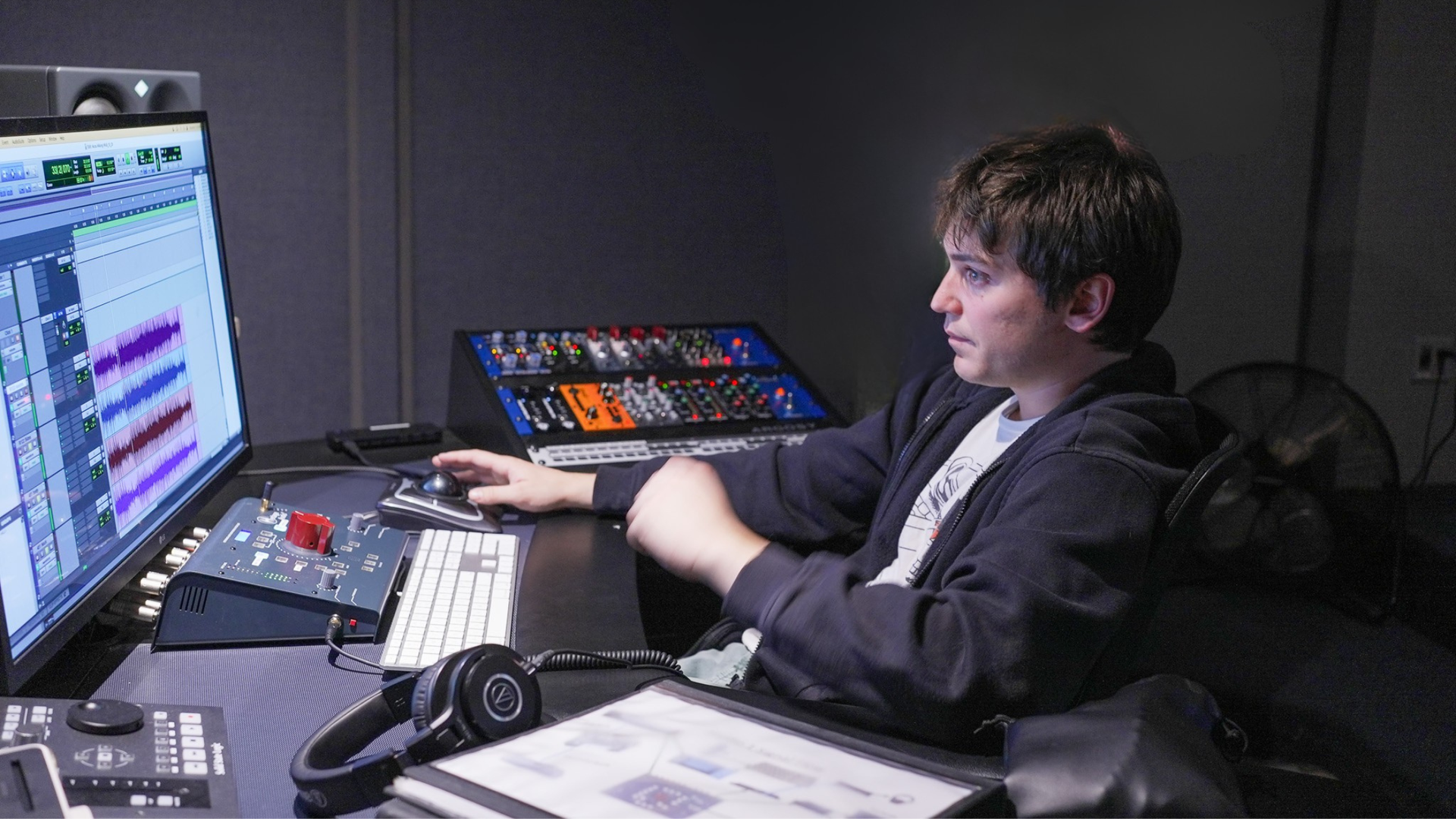 A man in a recording studio, seated at a desk, working on audio software.