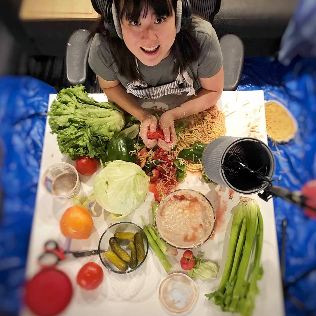 Person preparing a colorful salad at a table with lettuce, tomatoes, cucumbers, and bowls of ingredients