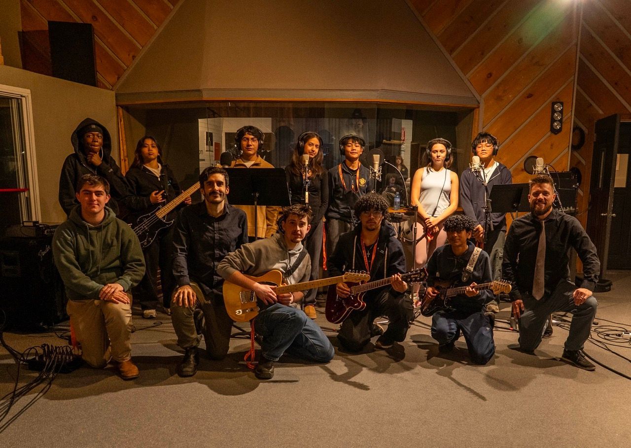 A group of people in a recording studio poses with guitars and other musical equipment.