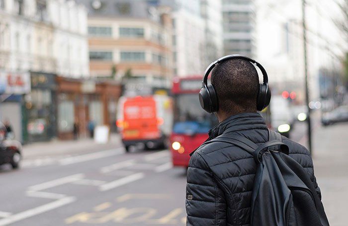 A man wearing headphones and a backpack is walking down a city street.