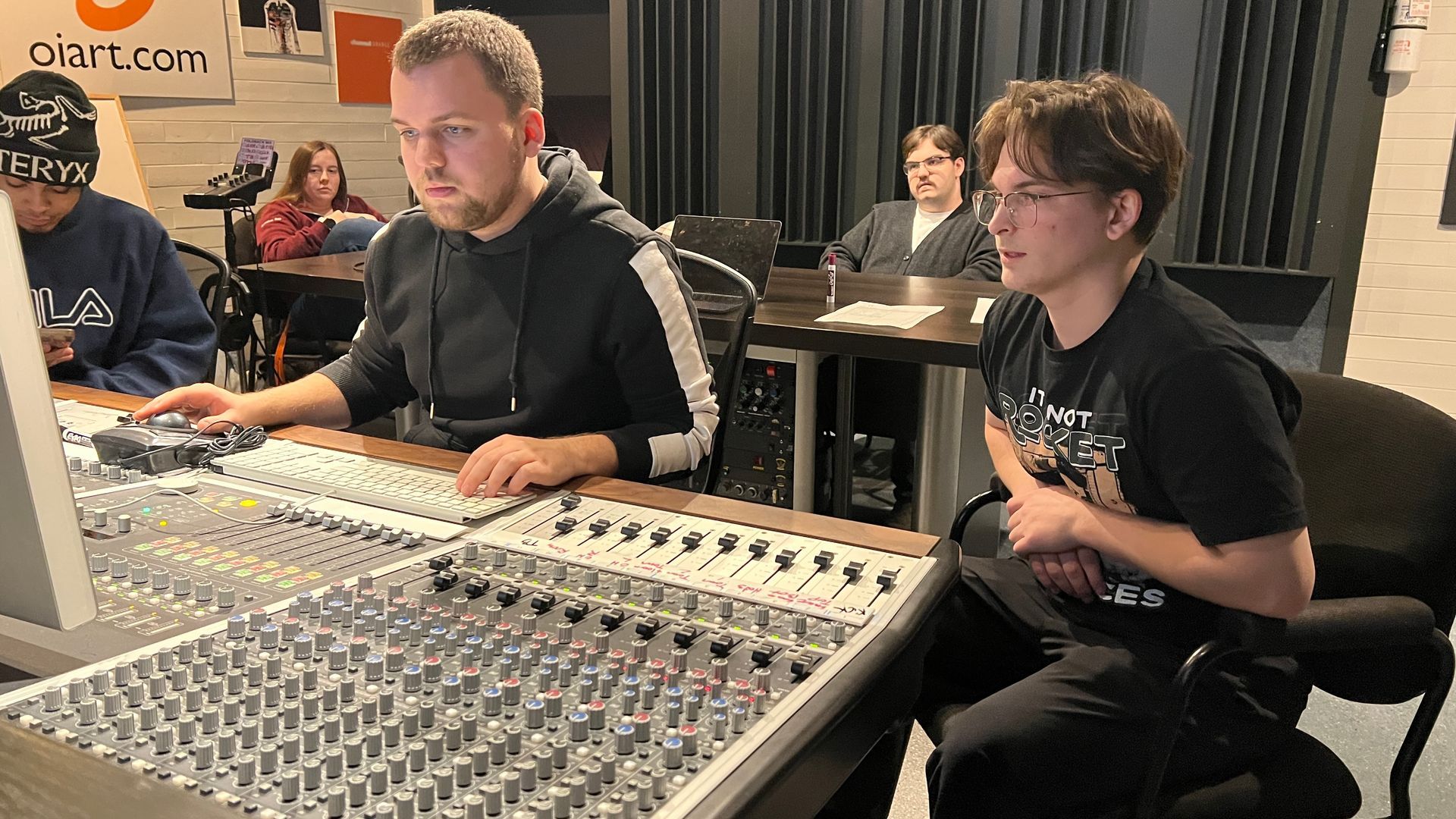 Avery Szumlanski & another student operating a large audio mixing console in a recording studio