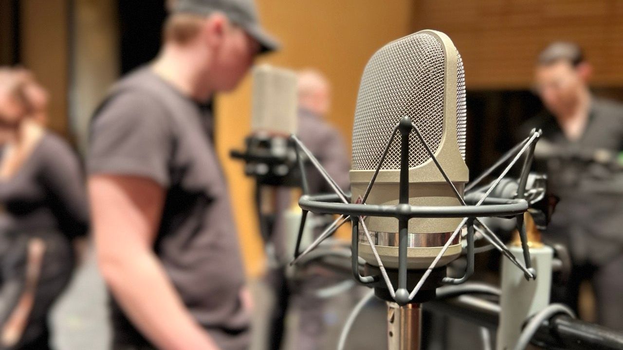 A student stands in front of a microphone in a recording studio