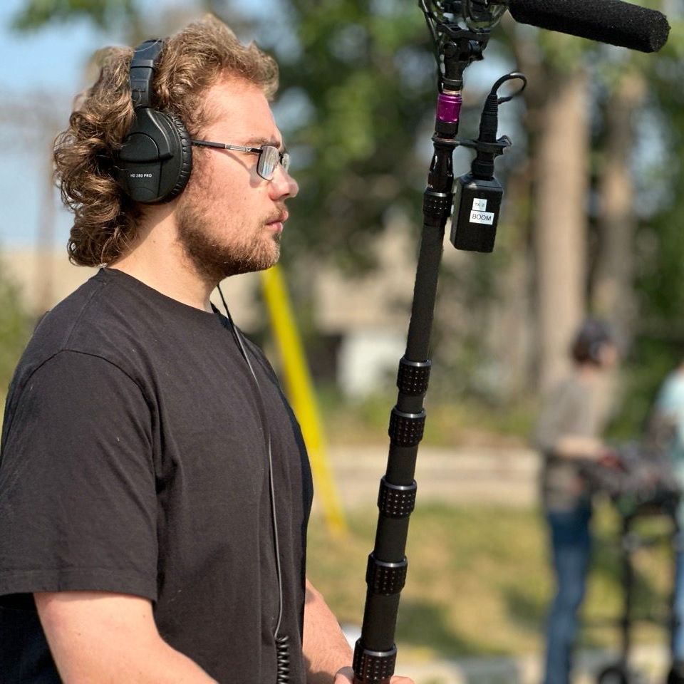 A man wearing headphones and glasses is holding a microphone on a pole