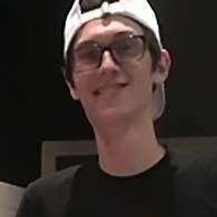 A young man wearing glasses and a hat is smiling for the camera.
