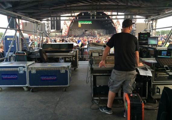Andrew Brown in a black shirt is standing behind the stage mixing audio.