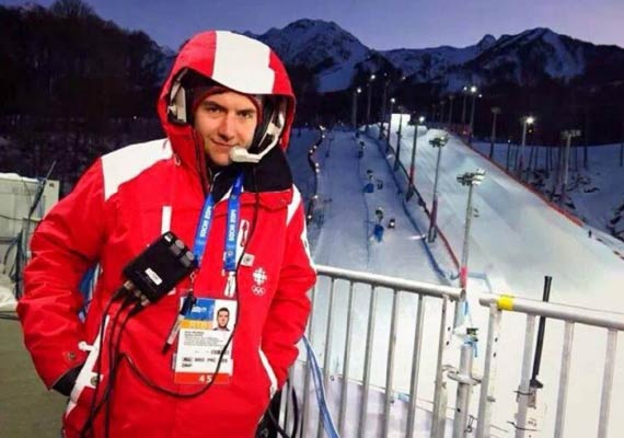 Bryan Moreau in a red jacket is standing in front of a snowy mountain.