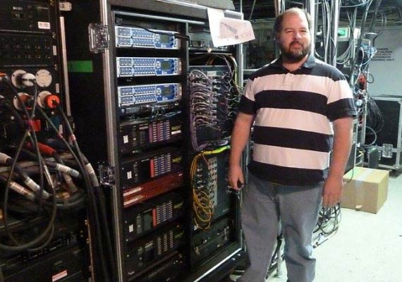 Craig Kadoke in a striped shirt stands in front of a server rack.
