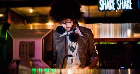 A man wearing headphones is playing music in front of a shake shack sign.