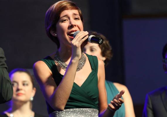 Marla Kishimoto singing into a microphone on stage, wearing a green dress and silver necklace.