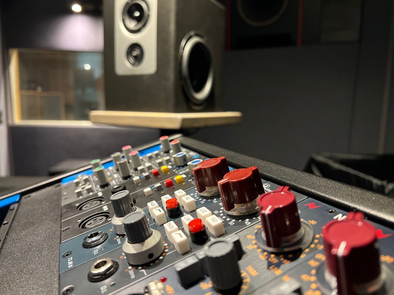 Close-up of a mixing console with red knobs in a recording studio, speakers visible in the background.