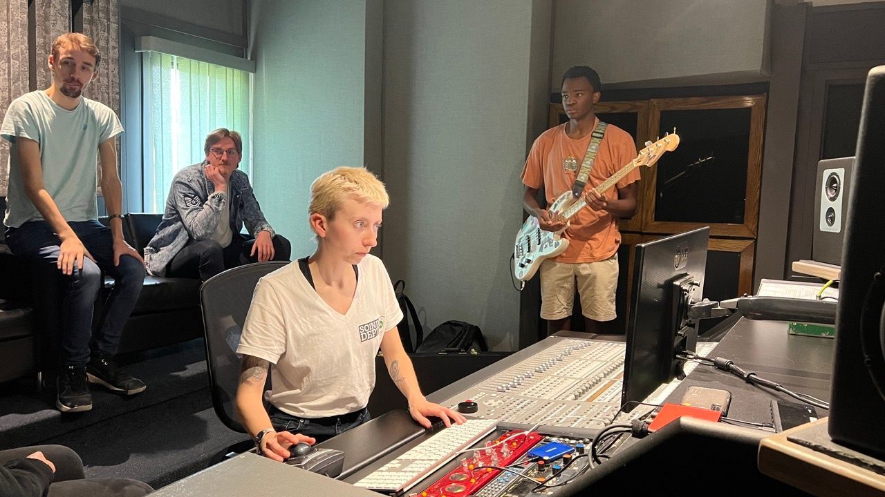 A group of people are standing around a desk in a recording studio.