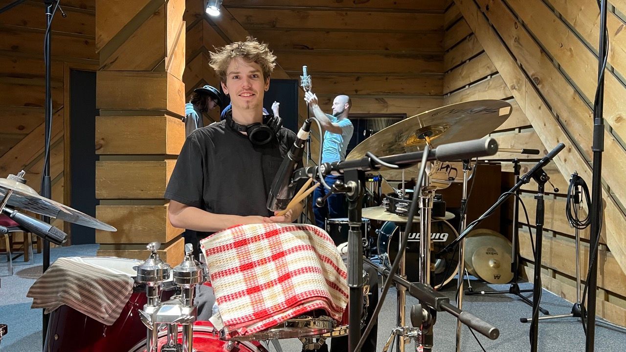 A young man is playing drums in a wooden room.