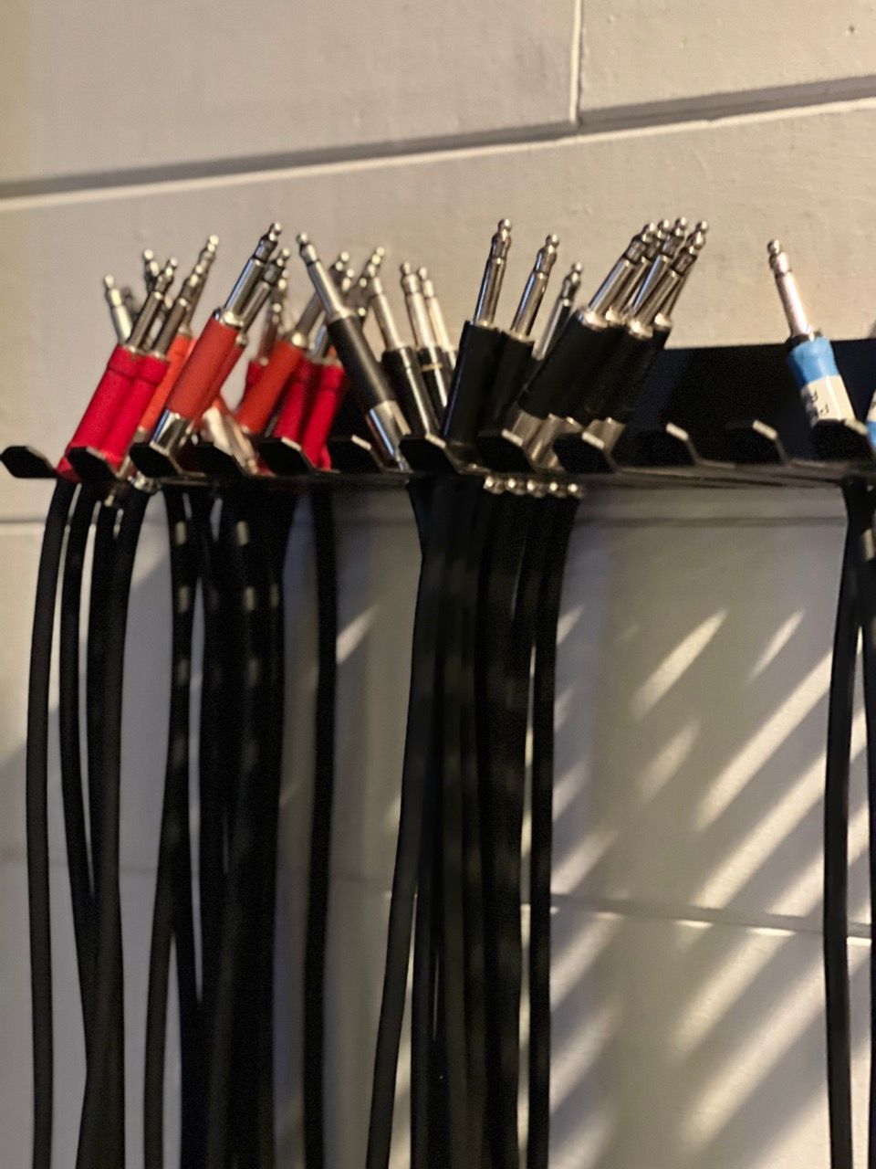 Black and colorful audio cables plugged into a black holder on a white wall.