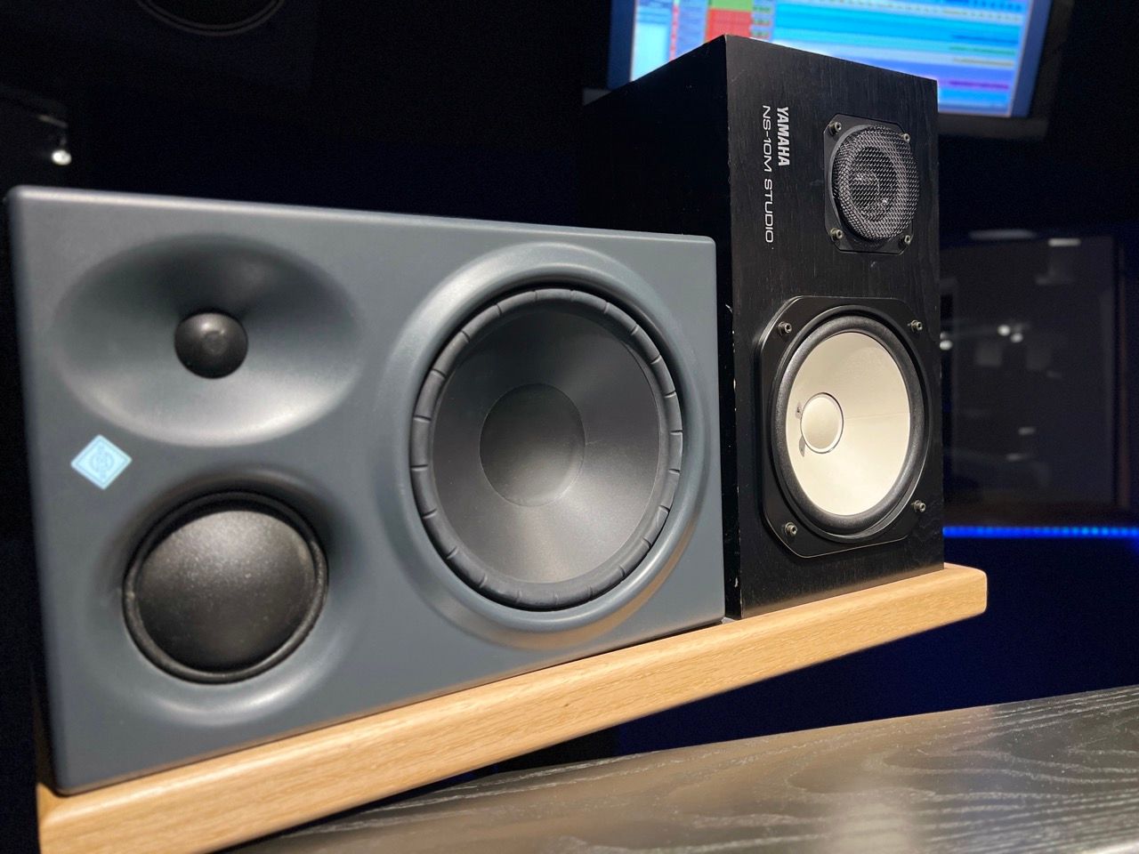 Two studio monitor speakers on a wooden shelf; gray and black.