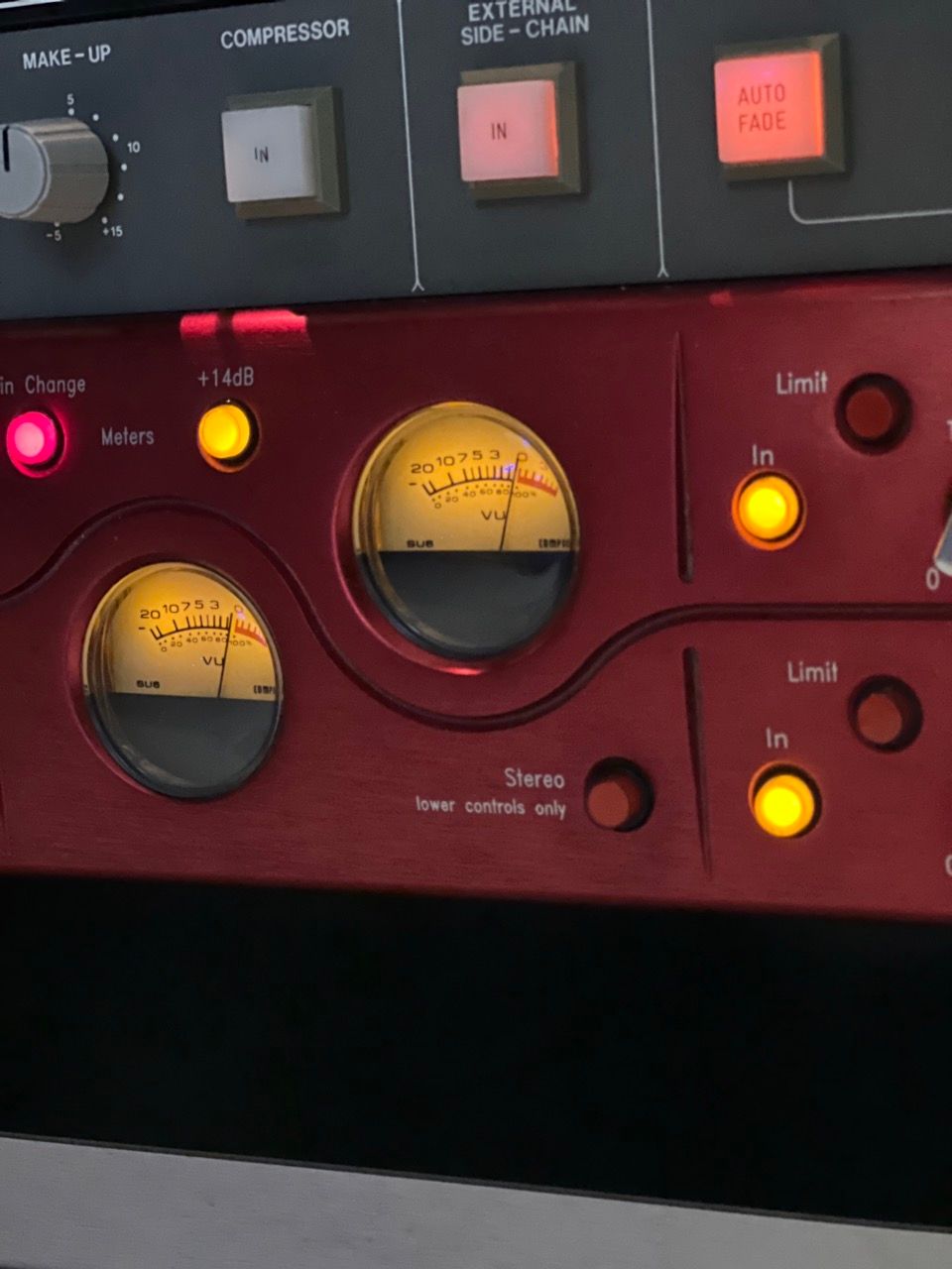 Close-up of a red audio compressor and limiter unit with illuminated meters and buttons.