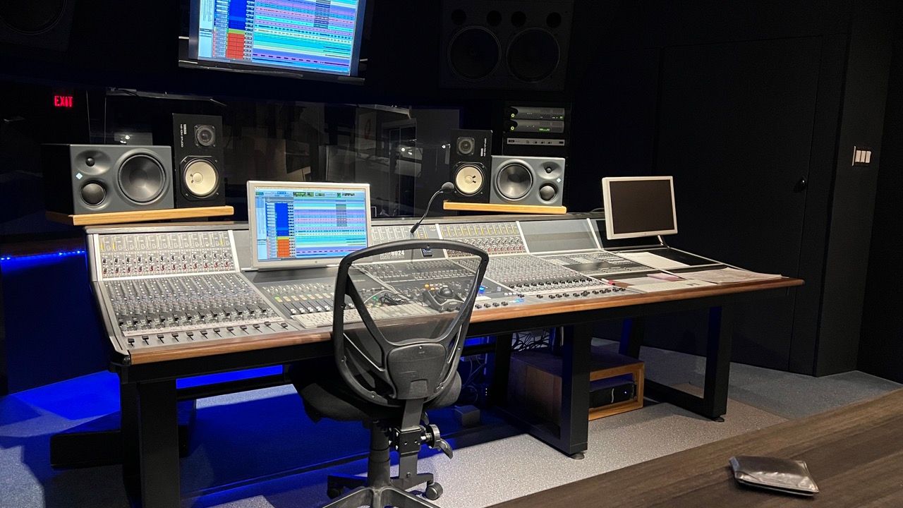 Recording studio with mixing console, monitors, computer screens. Dark room with blue lighting.