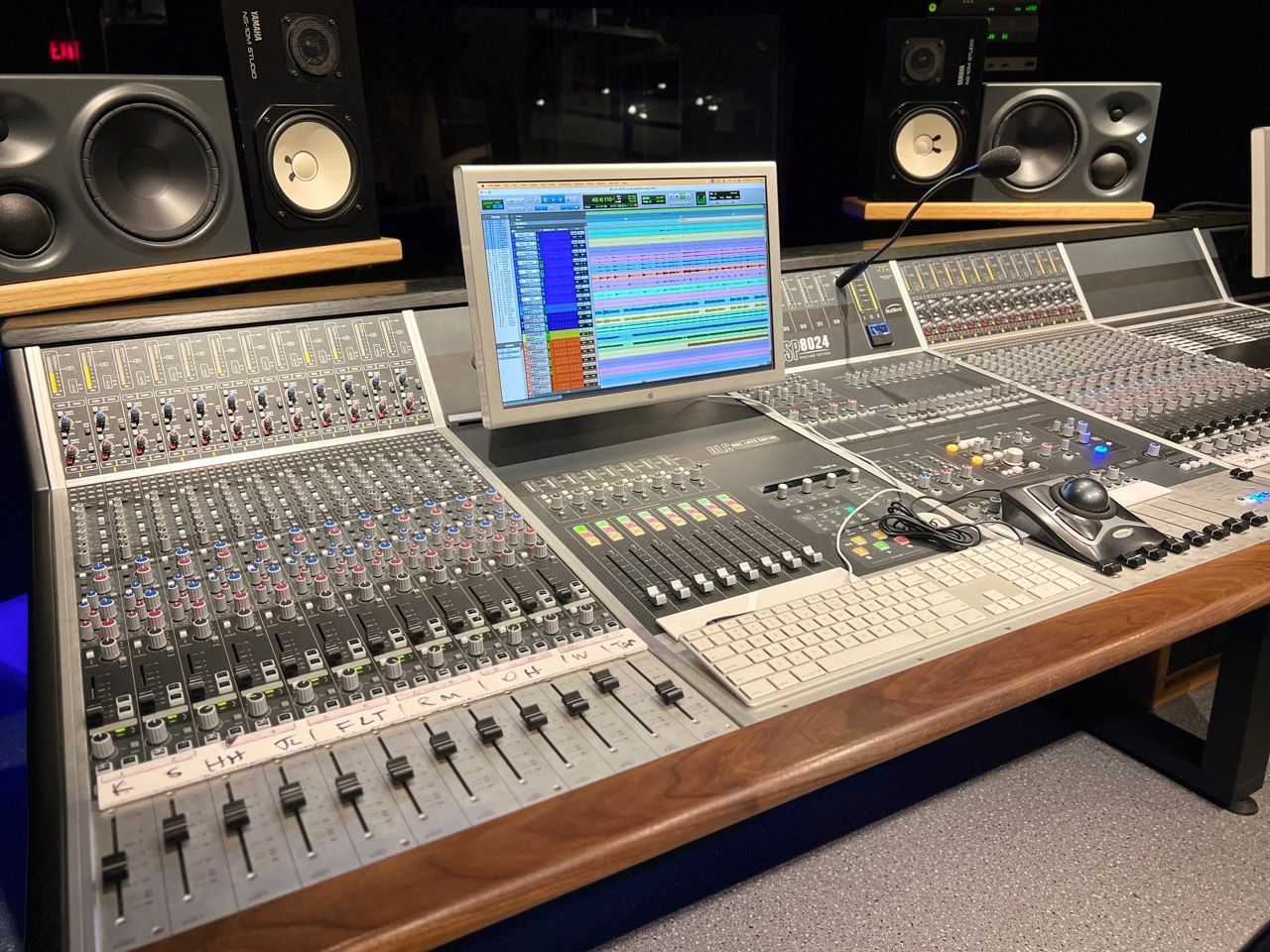 Recording studio console with multiple faders, a computer monitor displaying audio waveforms, and studio monitors.