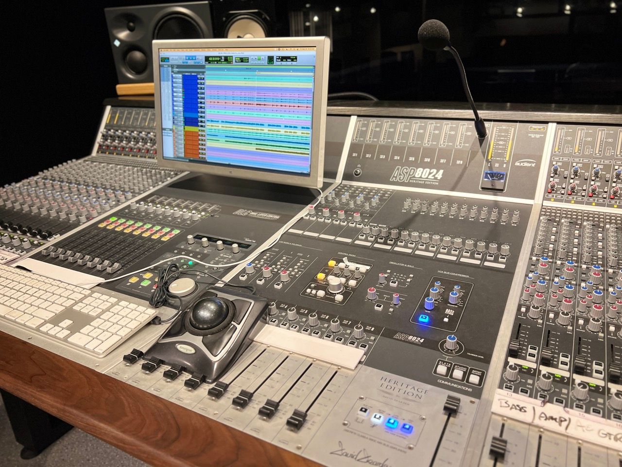 Recording studio control console with computer display, mixing board, microphone, and speakers.
