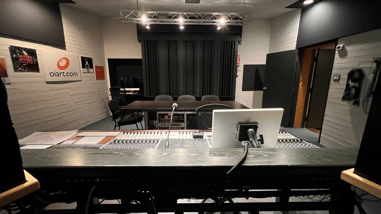 Recording studio interior. Dark desk with soundboard, computer monitor, behind chairs and curtains.