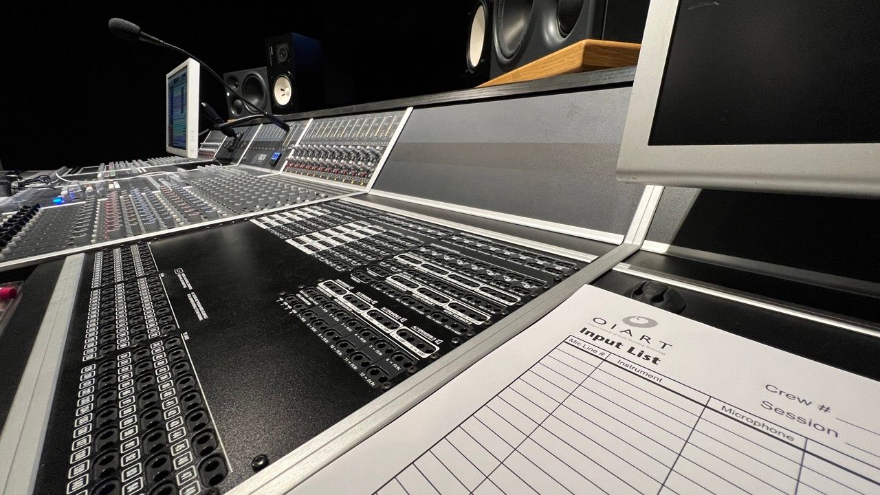 Recording studio control desk with monitors, speakers, and paperwork.