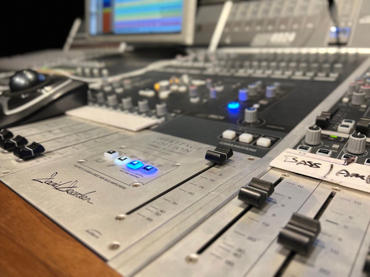 Close-up of a sound mixing console with sliders, knobs, and lit buttons in a recording studio.