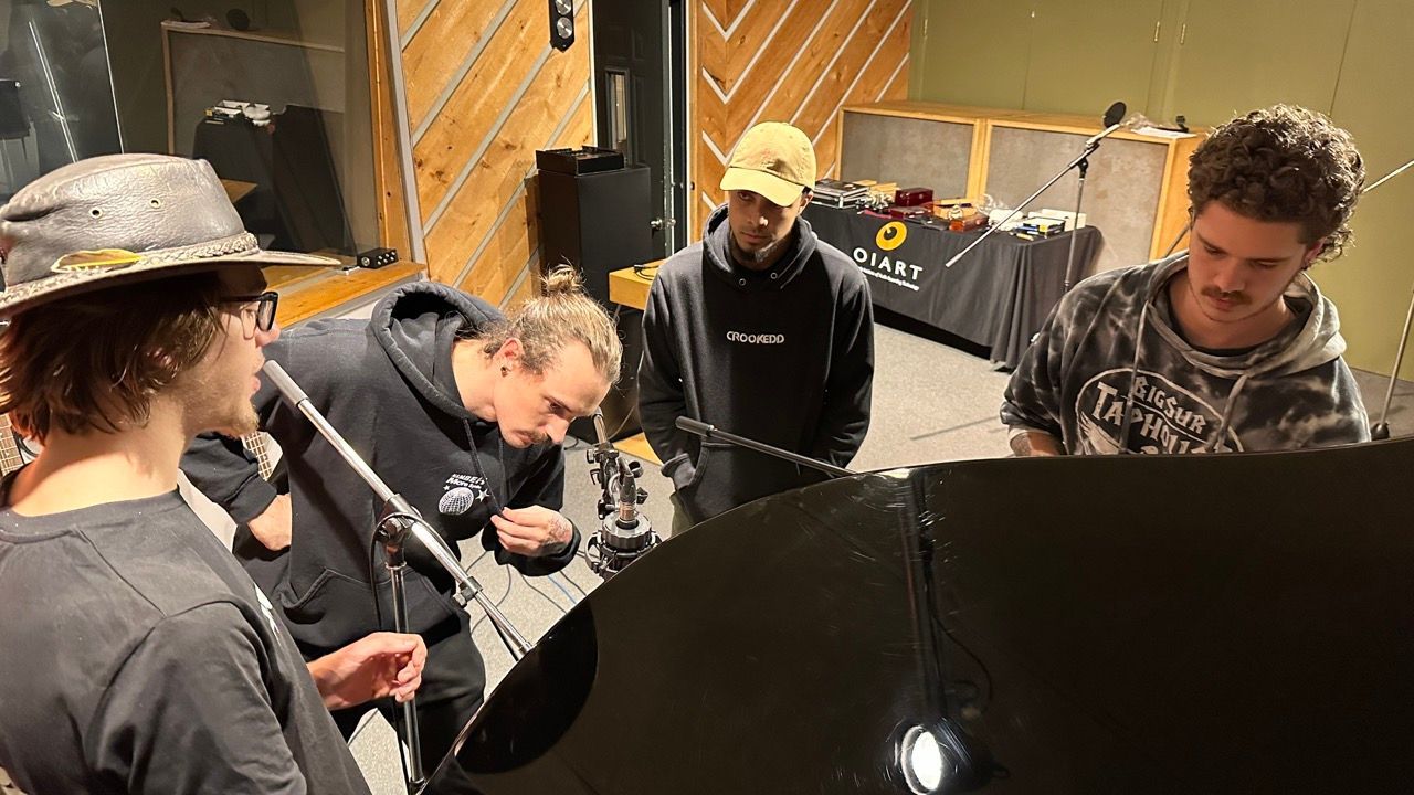 Four people gather around a grand piano in a recording studio, examining it.