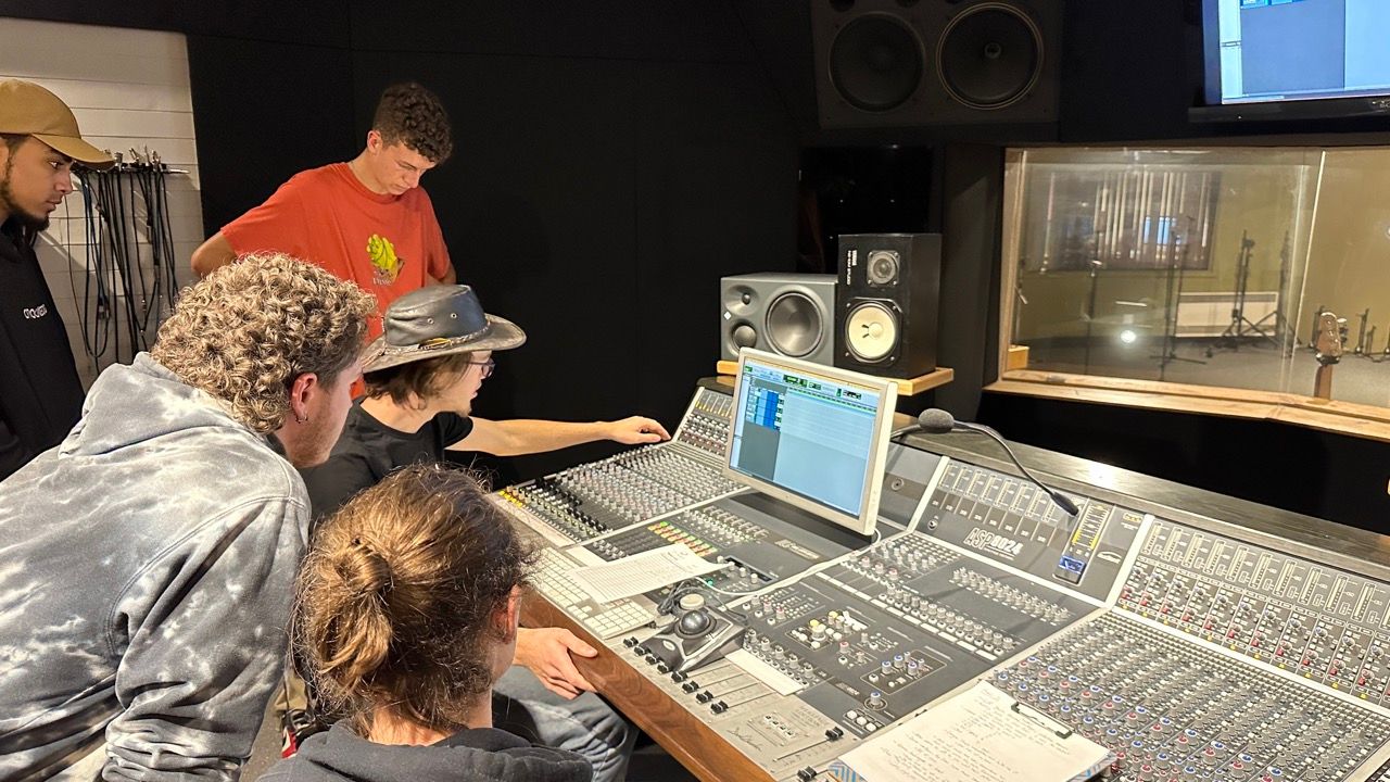Five people in a recording studio around a mixing console, looking at a computer screen.