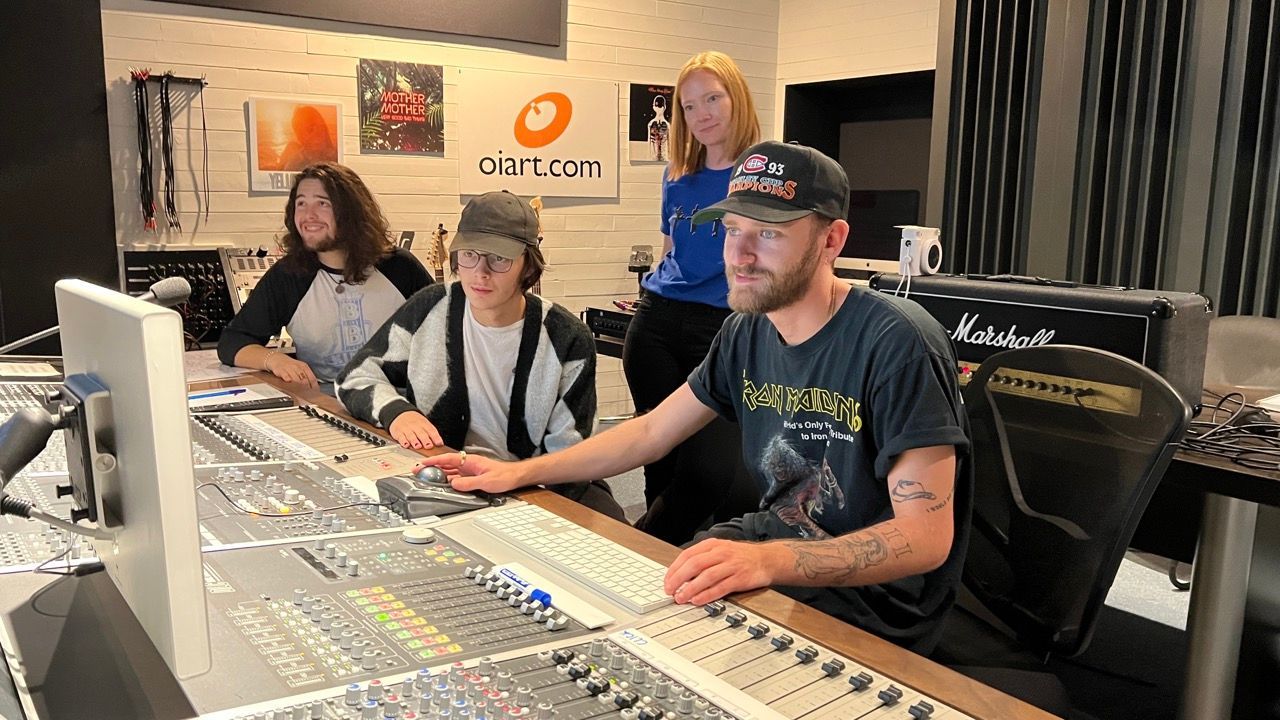 Four people in a recording studio: two men and two women. One man operates the mixing board.