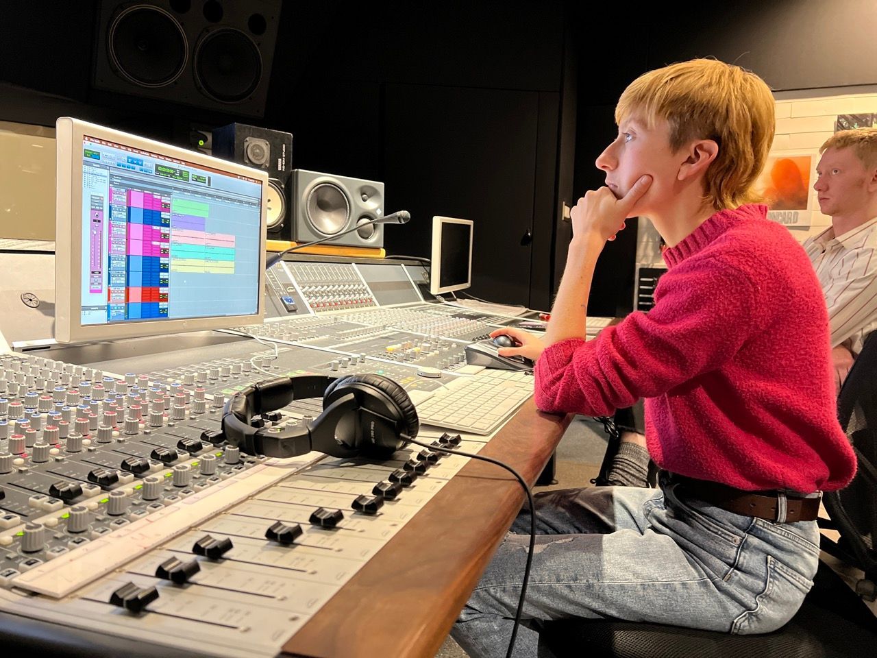 Person editing audio on a mixing console in a recording studio, looking intently at a computer screen.