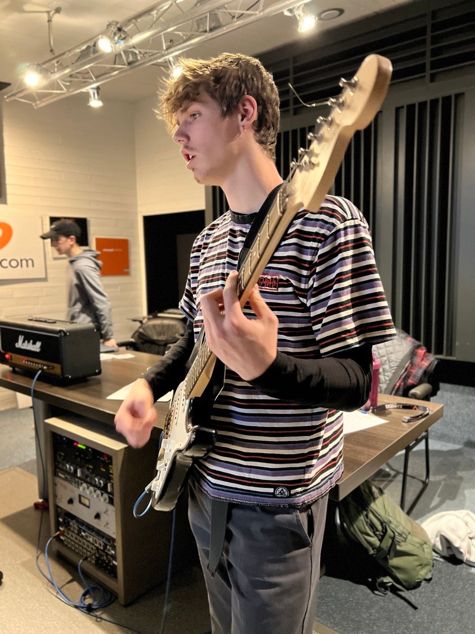 A person playing electric guitar in a studio, wearing a striped shirt.