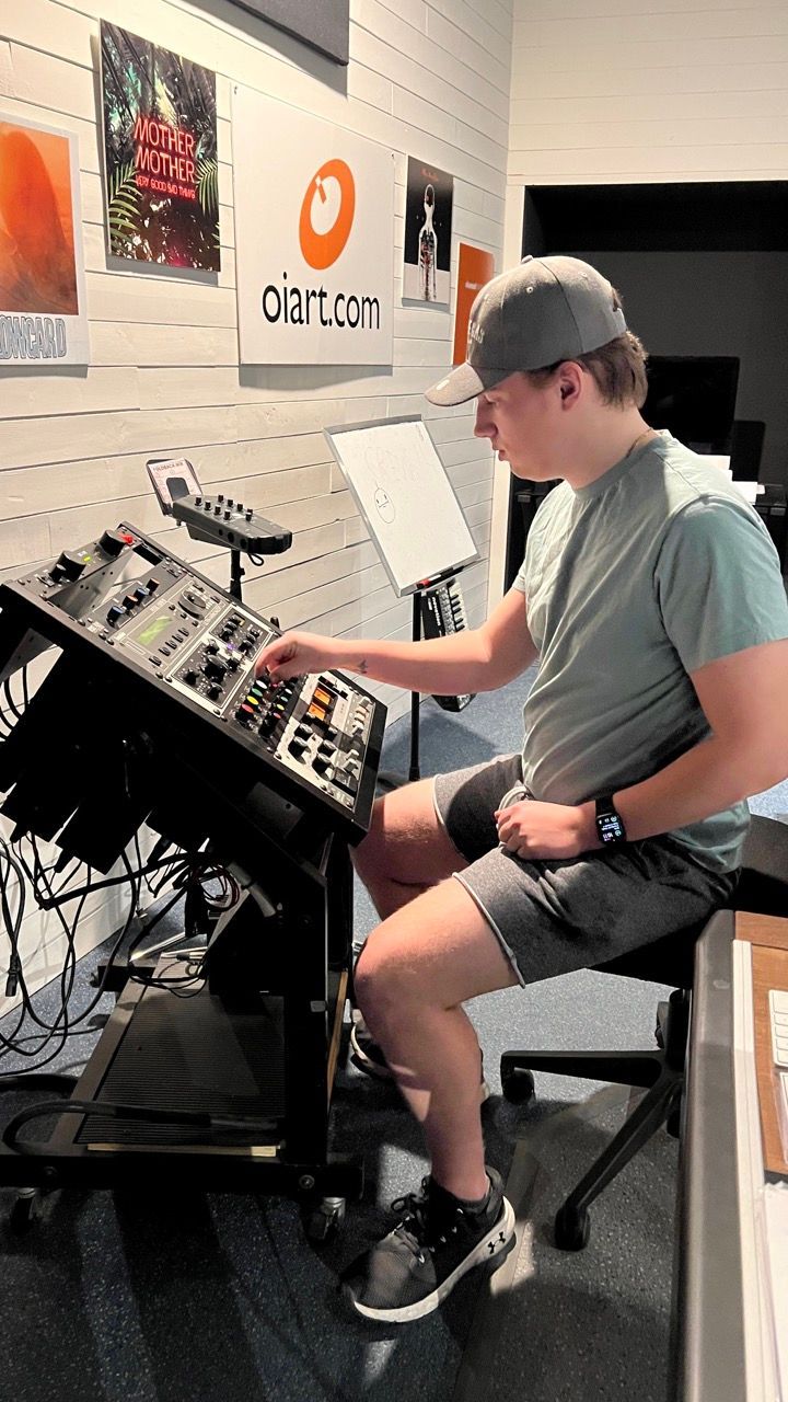 A person wearing a cap is operating a sound mixing console in a studio.