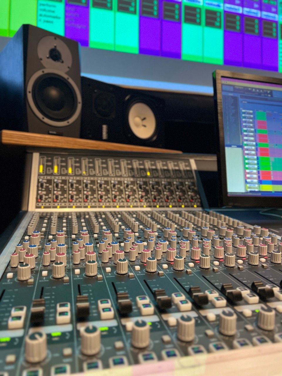 A mixing board with a laptop and speakers in the background