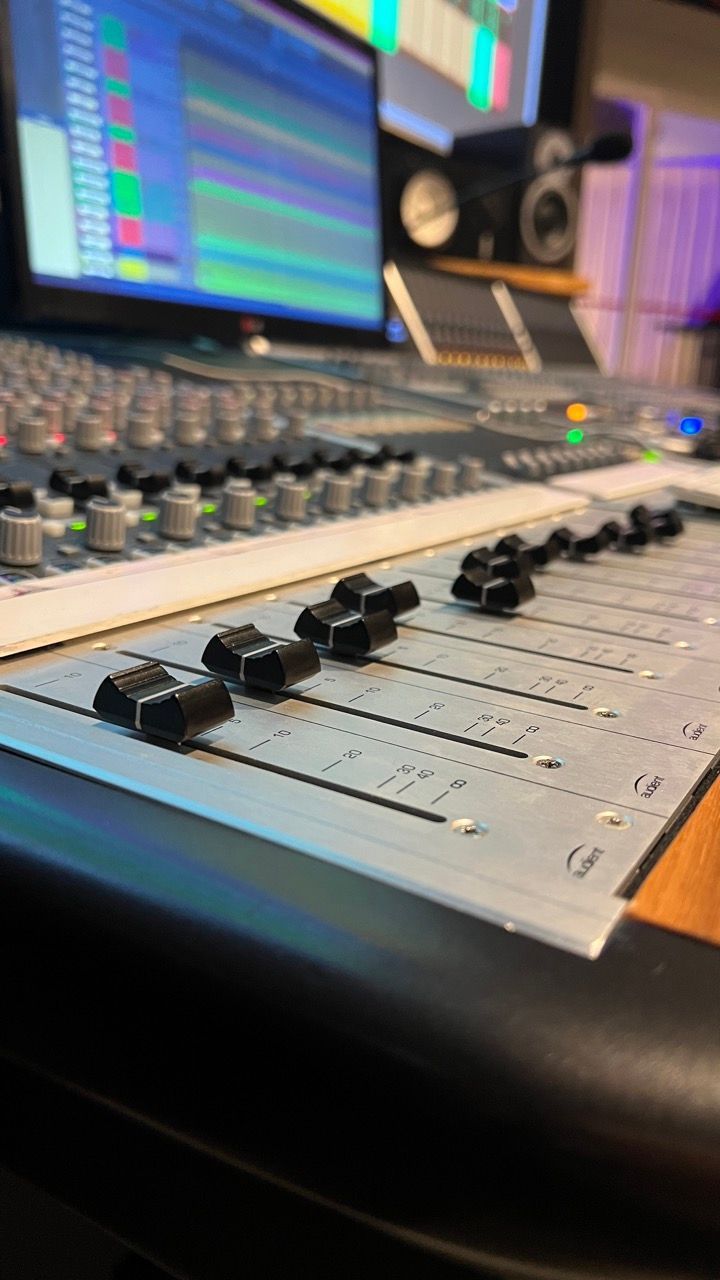 A close up of a mixer in a recording studio with a computer in the background.