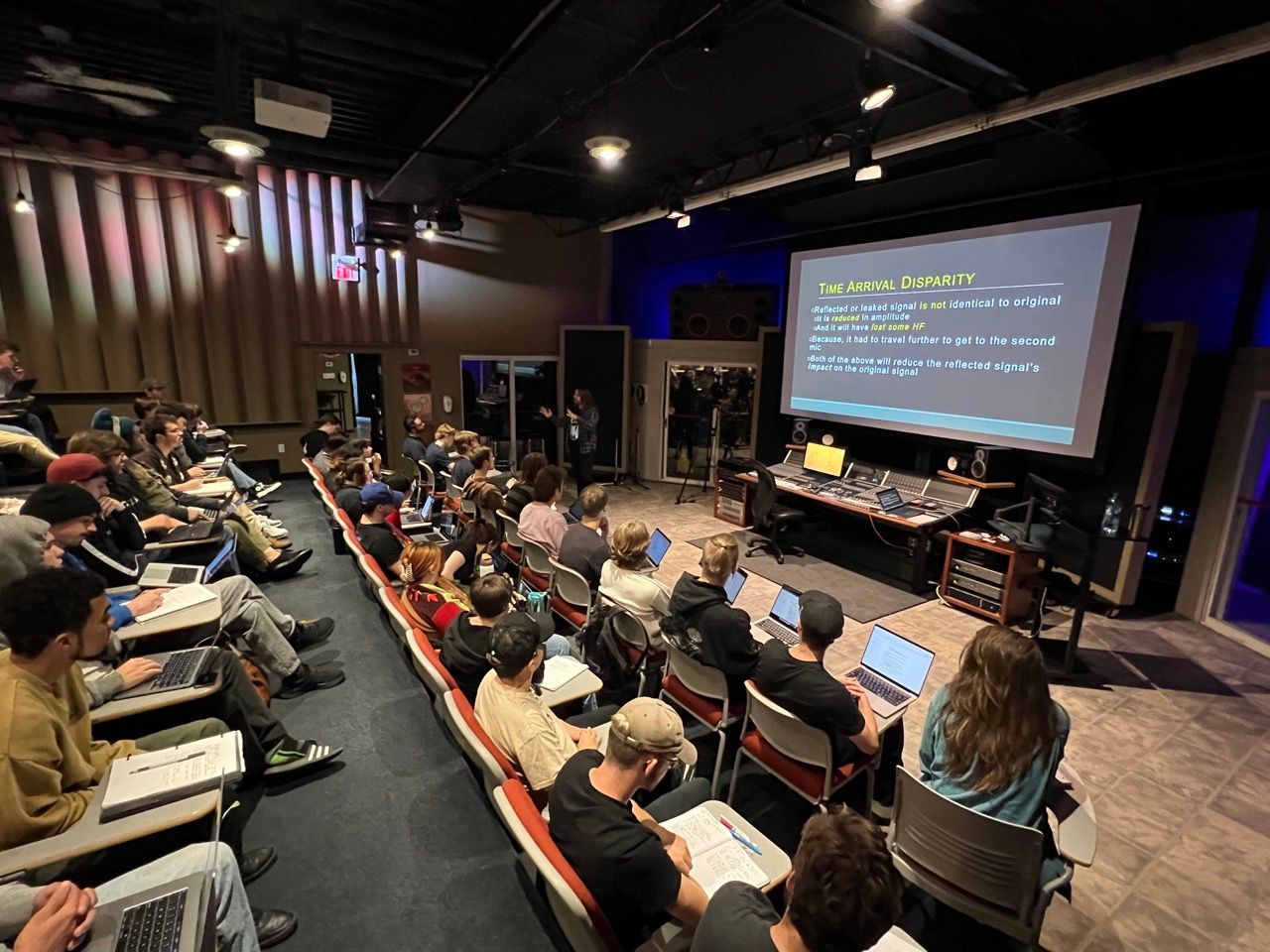 A large group of people are sitting in a lecture hall watching a presentation.