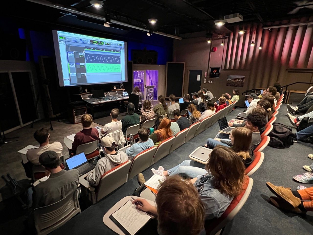A large group of people are sitting in an auditorium watching a presentation.