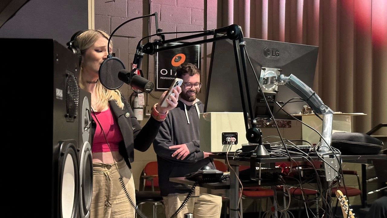 A man and a woman are singing into microphones in a studio.