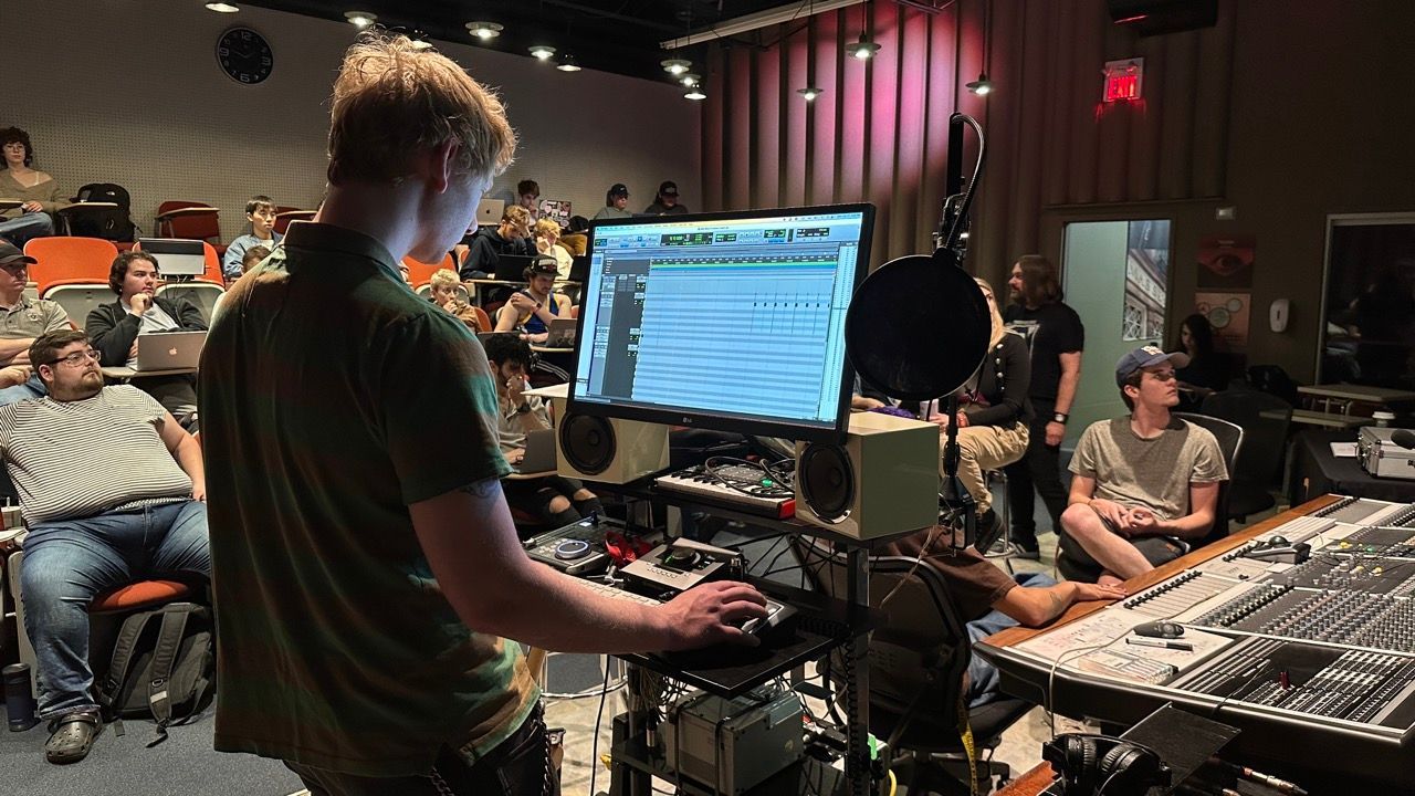A man is standing in front of a computer screen in a recording studio.