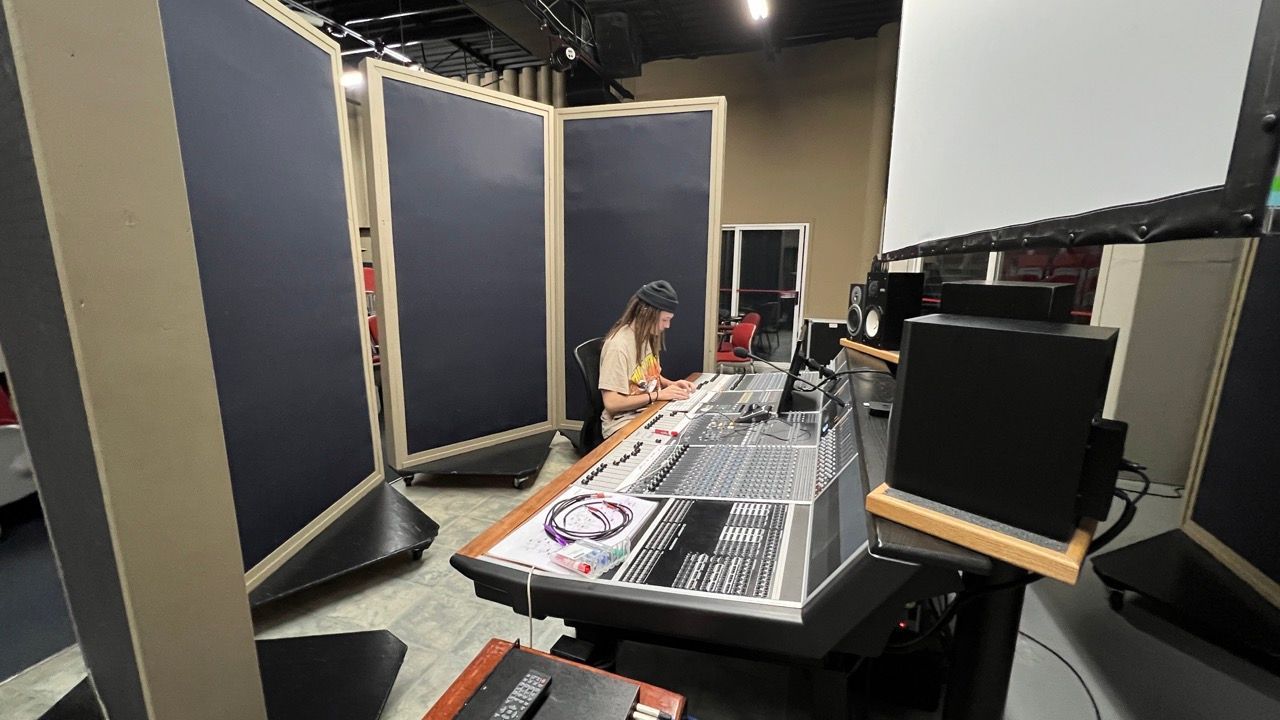 A woman is sitting at a desk in a recording studio.