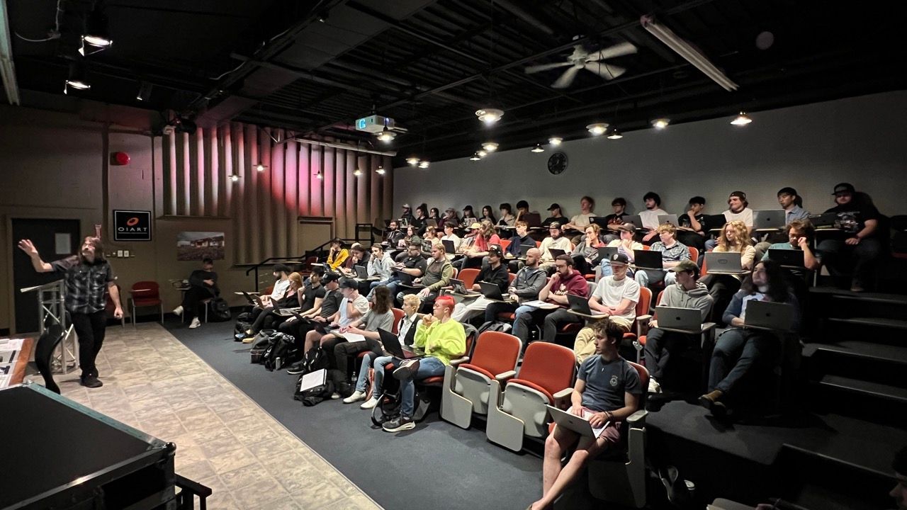 A man is standing in front of a large audience in an auditorium.