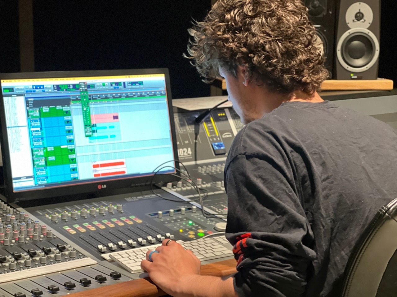 Person at a mixing console in a recording studio, focused on a computer screen displaying audio tracks.