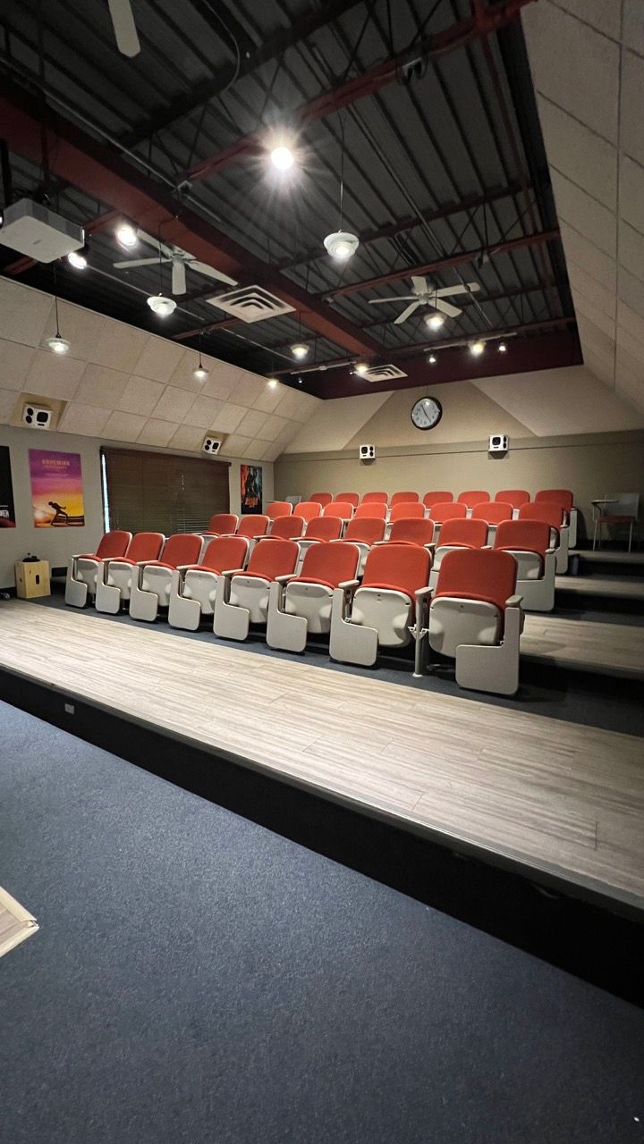 A large auditorium with rows of red chairs and a stage.