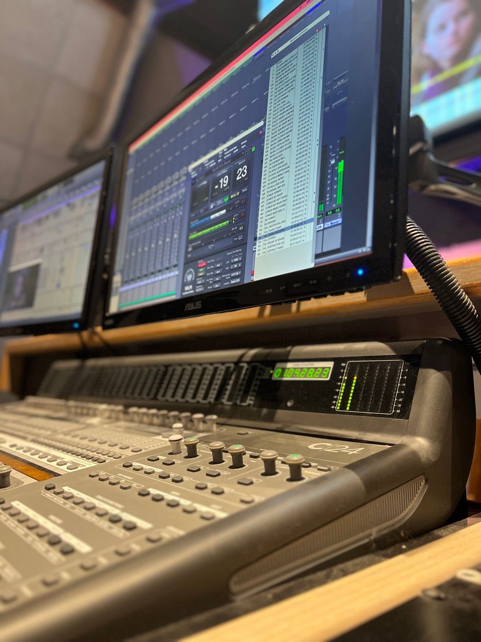 A mixer is sitting on top of a wooden desk next to three monitors.