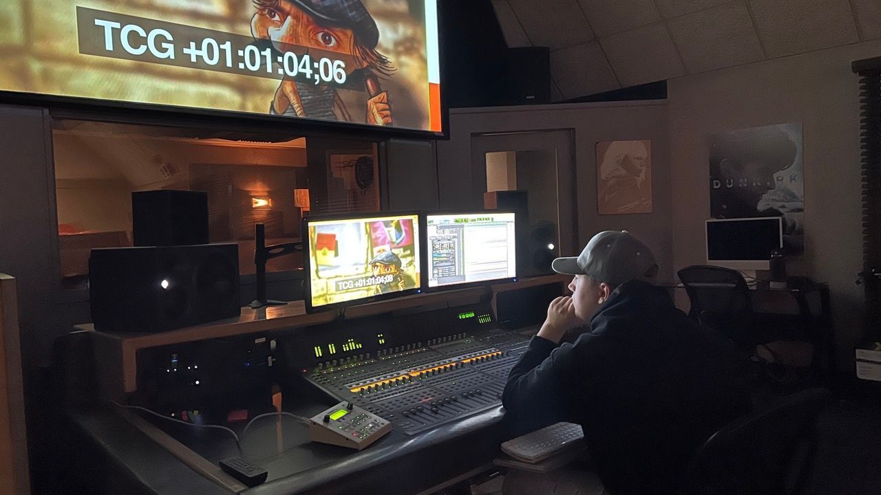 A man is sitting at a desk in front of a large screen.