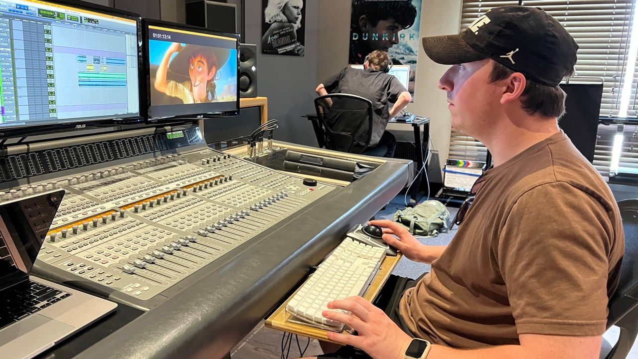 A man is sitting in front of a mixer in a recording studio.